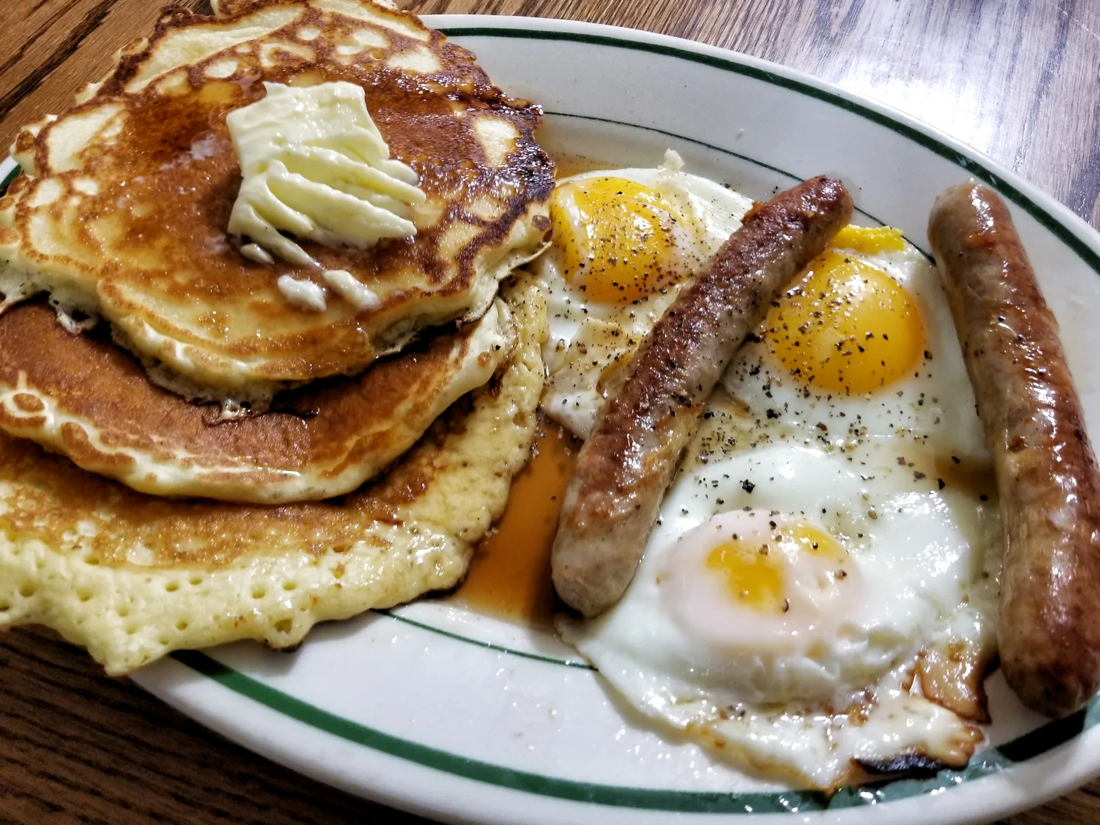 Pancakes with butter, fried eggs and sausage links on a diner plate.