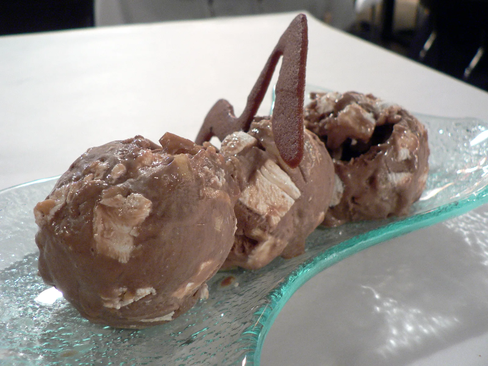 Three scoops of rocky road ice cream with a chocolate garnish on a glass plate.