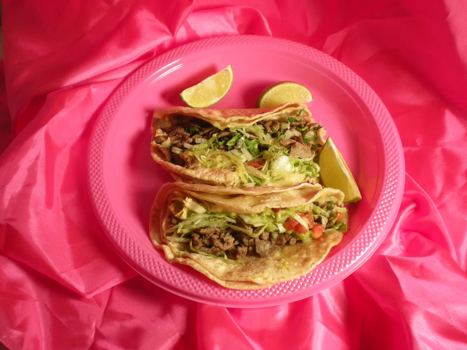 Steak tacos with lettuce, guacamole and lime on a pink plate at a taqueria in New York, a restaurant not on this list.