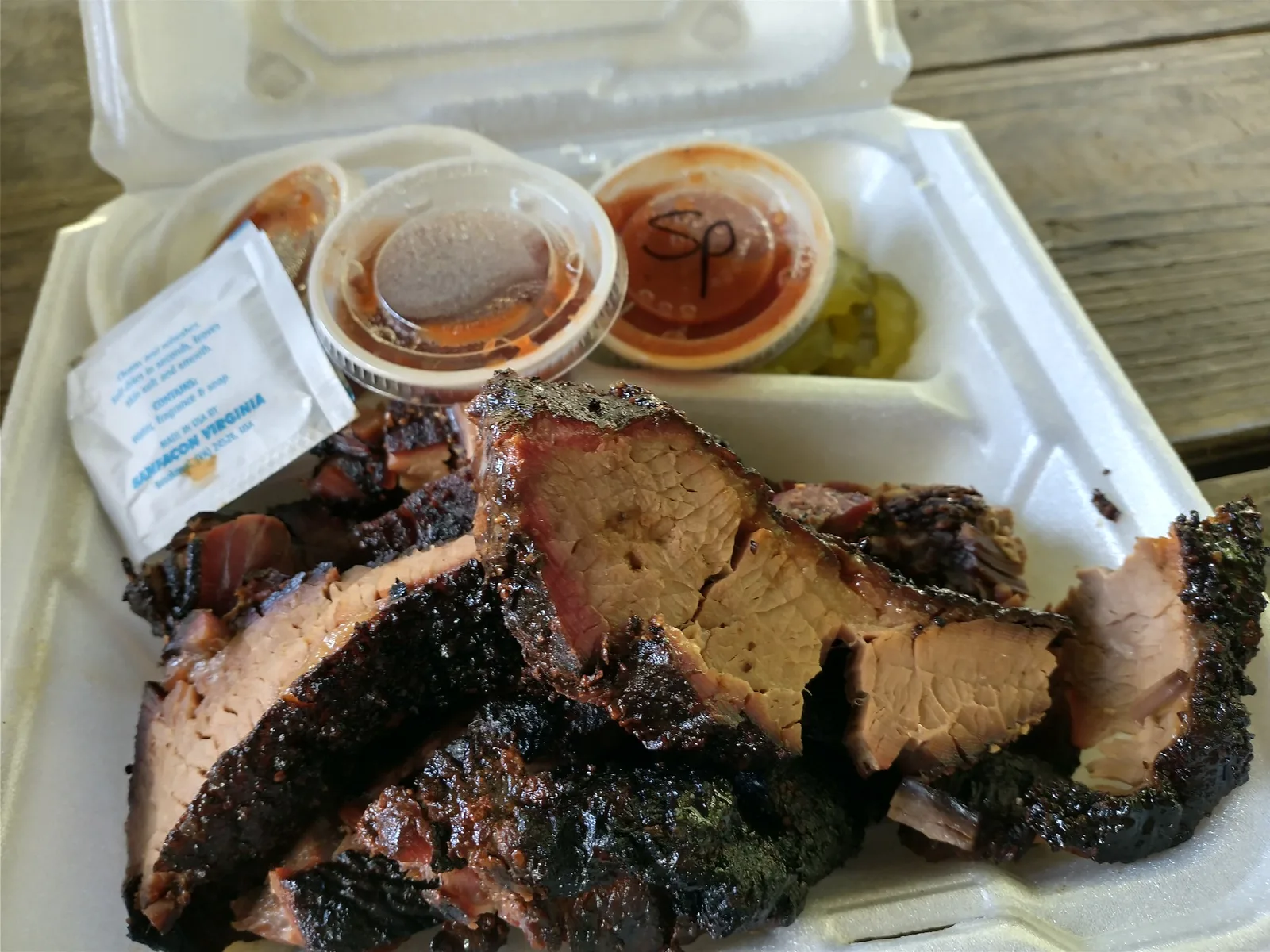 Sliced brisket with sauce cups and pickles in a takeout box from Blue Door Smokehouse in Lexington.