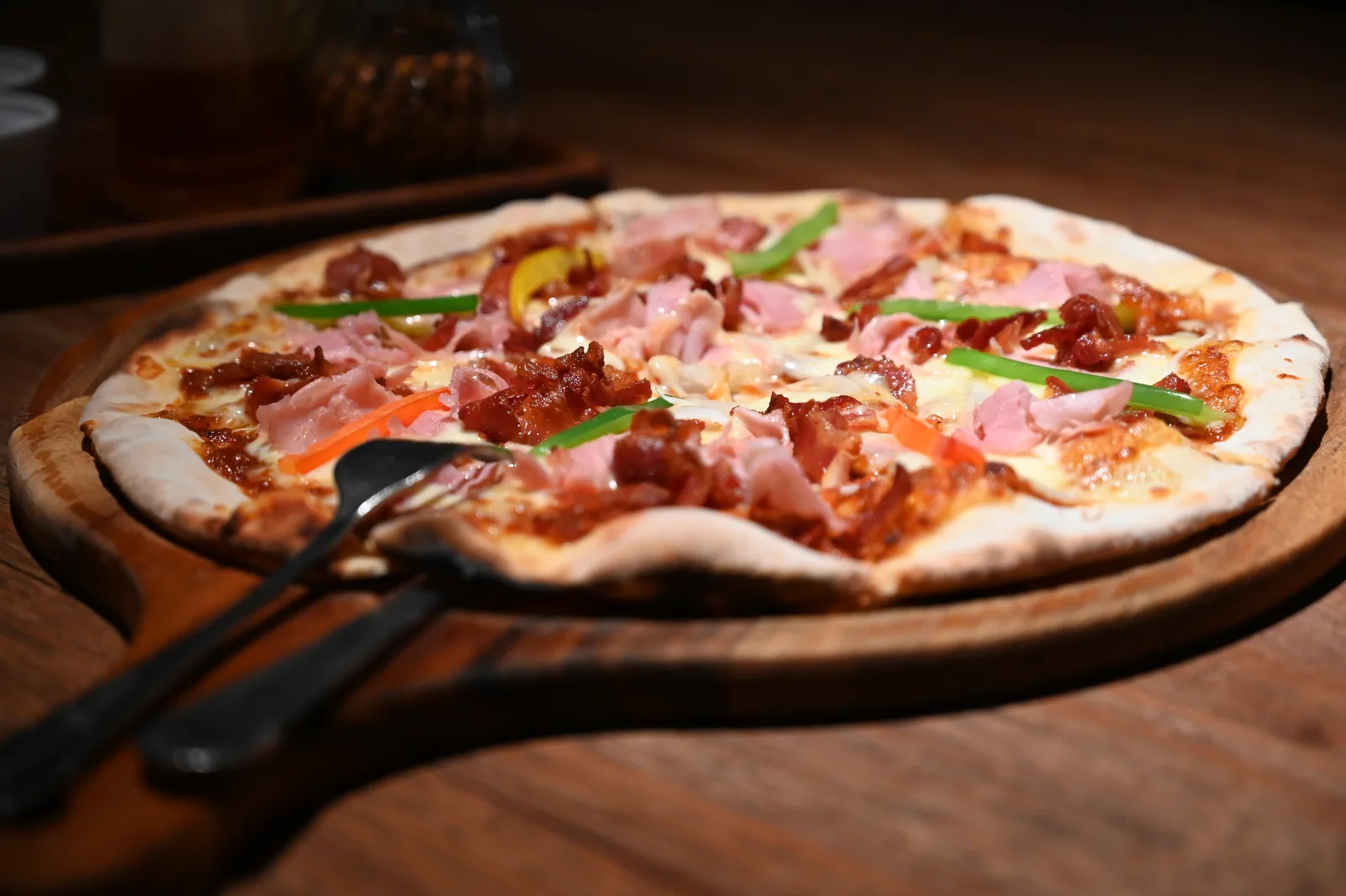 A wood-fired pizza topped with ham, peppers and melted cheese, ready to slice.